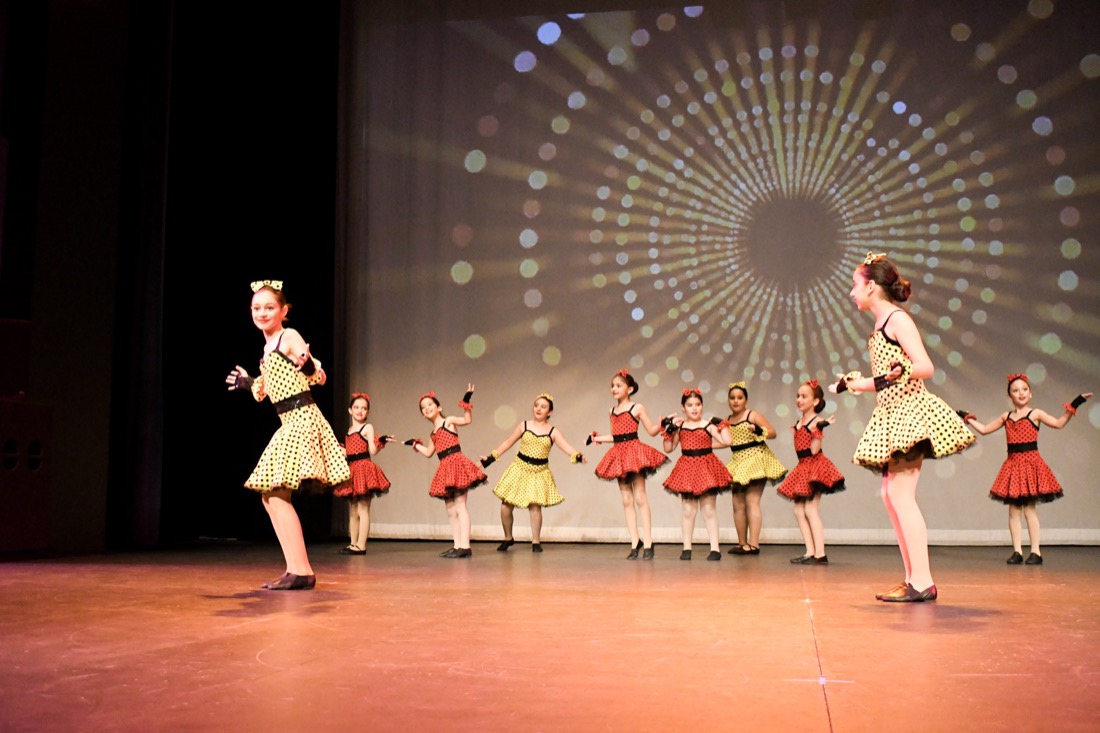 A dance ensemble performing in red and yellow polka-dot costumes on stage.